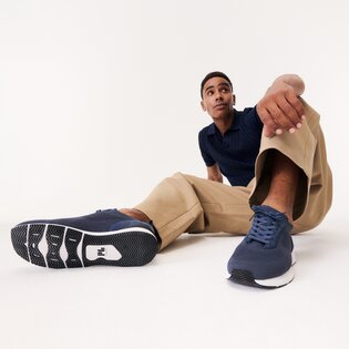 Un homme est assis de manière détendue sur le sol, porte un pantalon beige, un haut bleu et des baskets bleu foncé. Les chaussures sont visibles au premier plan de l’image. | © Gabor Shoes GmbH, Allemagne