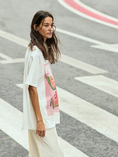 Une femme traverse un passage piéton et porte un t-shirt blanc avec un imprimé coloré ainsi qu’un pantalon clair. La rue présente des marquages voyants. | © Gabor Shoes GmbH, Allemagne