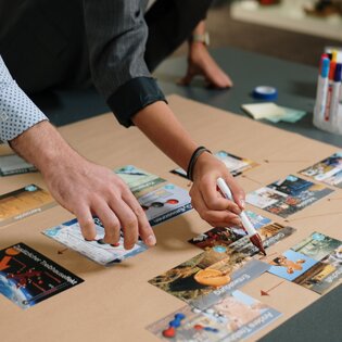 Deux personnes travaillent à une table et organisent des cartes d’information, une personne tient un stylo. | © Gabor Shoes GmbH, Allemagne