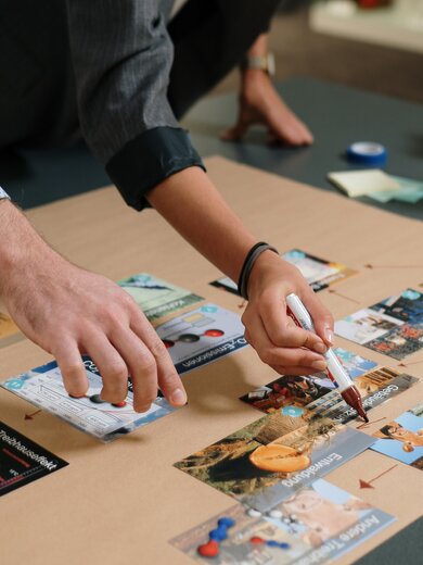 Deux personnes travaillent à une table et organisent des cartes d’information, une personne tient un stylo. | © Gabor Shoes GmbH, Allemagne