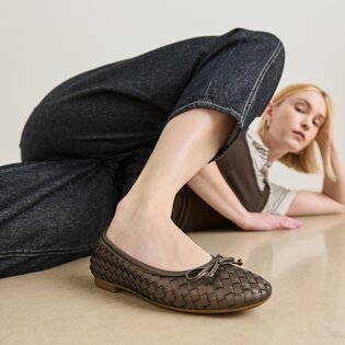Une femme est allongée de manière détendue sur le sol et porte des ballerines tressées marron foncé ainsi qu’un jean foncé. | © Gabor Shoes GmbH, Allemagne