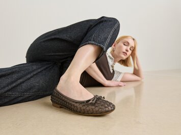 Une femme est allongée de manière détendue sur le sol et porte des ballerines tressées marron foncé ainsi qu’un jean foncé. | © Gabor Shoes GmbH, Allemagne
