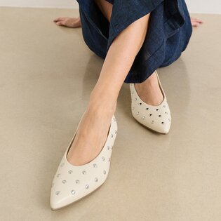 Une femme est assise par terre et porte un pantalon bleu foncé ainsi que des escarpins beiges pointus avec des clous argentés. | © Gabor Shoes GmbH, Allemagne