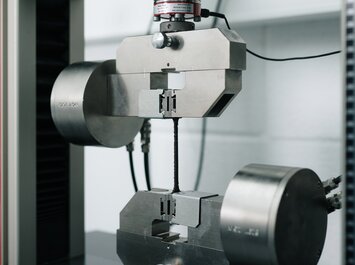 Une machine d’essai en métal maintient une fine bande d’essai entre deux pinces pour un test de traction. | © Gabor Shoes GmbH, Allemagne