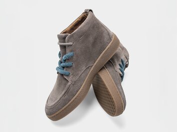 Grijze dames-boots van suède met lichtbruine zool en blauwe veters, vrijstaand tegen een witte achtergrond. | © Gabor Shoes GmbH, Duitsland