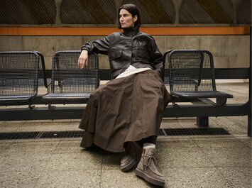 Een vrouw zit op een bank in een metrostation, draagt een bruine leren jas, een lange bruine rok en beige Gabor-veterschoenen. | © Gabor Shoes GmbH, Duitsland