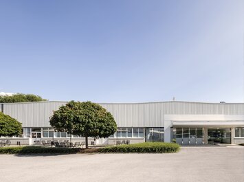 Vue extérieure d’un bâtiment industriel moderne avec des arbres et un ciel bleu.
