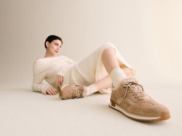 En kvinna ligger avslappnat på golvet mot en ljus bakgrund, bär en cremefärgad stickad klänning och beiga Gabor-sneakers med ljus sula. | © Gabor Shoes GmbH, Tyskland