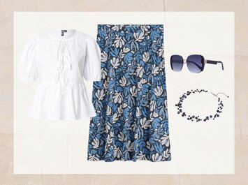 Une tenue composée d’un chemisier blanc à manches courtes bouffantes, d’une jupe jusqu’au genou avec un motif de feuilles bleu et blanc, de lunettes de soleil bleu foncé et d’un collier bleu assorti. Tous les éléments sont disposés côte à côte sur un fond clair. | © aboutyou.de 