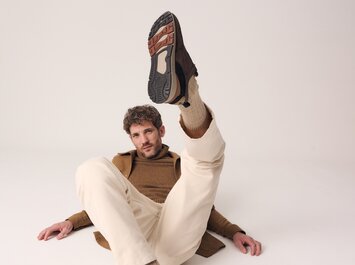 Un homme est assis par terre en pantalon clair et pull brun et tend une jambe vers le haut de manière à bien voir la semelle de la chaussure. L’arrière-plan est neutre et clair. | © Gabor Shoes GmbH, Allemagne