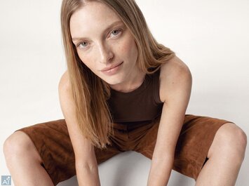 Une image générée par IA montrant une jeune femme assise de façon décontractée au sol, portant un haut marron foncé et un short marron. | © Gabor Shoes GmbH, Allemagne