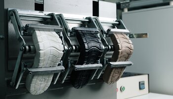 Three differently colored shoe soles are clamped in a testing machine. | © Gabor Shoes GmbH, Germany