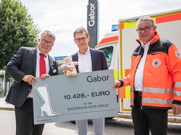 "Three people present a large Gabor donation check to the Bavarian Red Cross. " | © Gabor Shoes GmbH, Germany