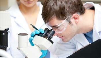Two people are working in the laboratory and examining something under the microscope. | © WavebreakMediaMicro