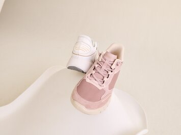 Gabor Women’s Shoes | Two FlexFlex women’s sneakers in pink and white on a light, curved surface against a neutral background. The white sneaker is photographed from the back, the pink one from the front. | © Gabor Shoes GmbH, Rosenheim