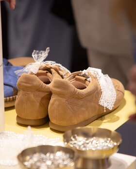 Ett par bruna sneakers från Gabor i mocka med vit spetsdetalj visas bakifrån på ett gult bord. | © Gabor Shoes GmbH, Rosenheim